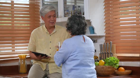 Asian senior couple drinking orange juice healthy food and using tablet online communication.