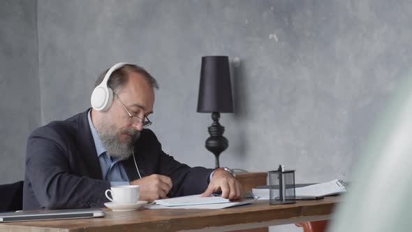 Elderly Businessman Listening to Music while Making Notes alt