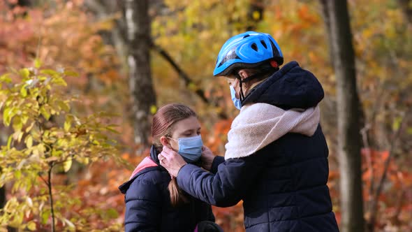 Mom puts on a medical mask and Bicycle helmet for her daughter in the fall