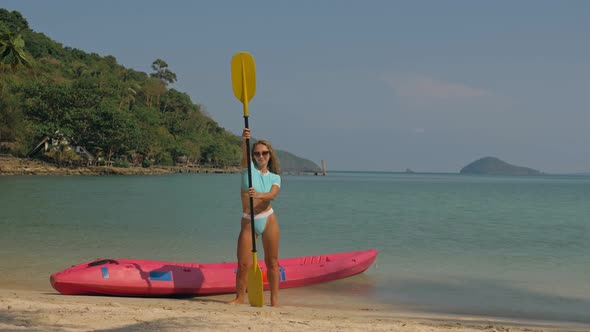 Pretty Young Sportswoman with Sunglasses and Swimsuit Holds Paddle Posing Near Pink Plastic Canoe on alt