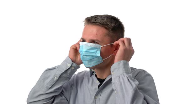 Young Man Wearing a Grey Shirt Putting on a Mask on a White Background