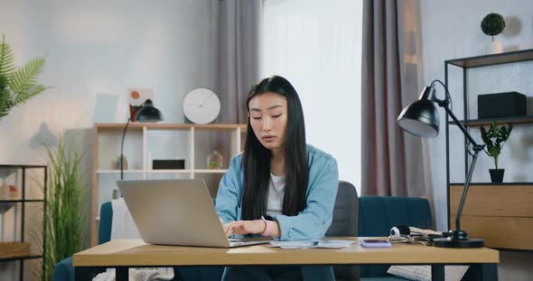 Asian Girl Sitting at the Computer at Home and Working Over Her University's Hometask alt