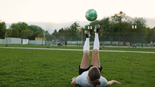 Woman Football Soccer Freestyler Practicing Tricks with Ball Laying on Grass in the Park at Sunset