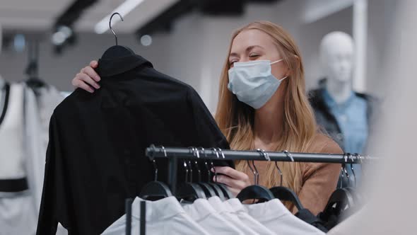 Caucasian Girl in Mask in Mall Chooses Clothes Young Beautiful Woman Enjoy Shopping at Discount alt