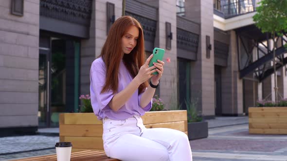 Portrait of Happy Playful Young Woman with Red Hair Making Selfie Photo By Phone Outdoors. alt