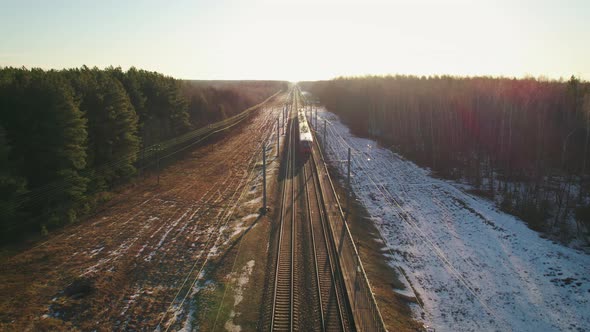 Passenger Train Passing Through the Forest on the Background of the Setting Sun alt