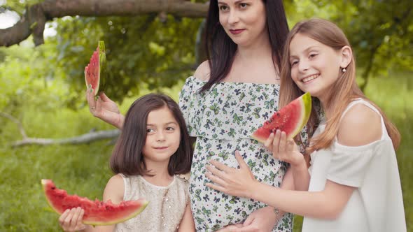 Pregnant Caucasian Woman and Her Two Pretty Daughters Standing Together in Hugs alt