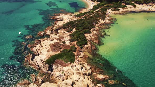 Aerial View of a Rocky Side of Karydi Beach Surrounded By Shallow Turquoise Water alt