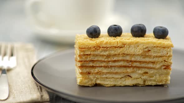 Napoleon Cake Decorated By Four Blueberries on Top of It. On Gray Plate. Blurred Cup Background and alt