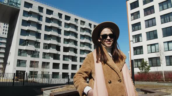 The Girl Adjusts Her Hat and Looks Into the Camera Against the Background of the Architecture