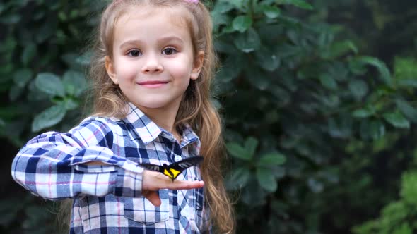 A Very Cute Girl Holds a Butterfly on Her Hand Turns to Frame and Smiles alt
