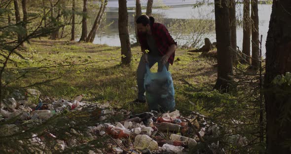 A Male Volunteer Collects Trash Scattered in the Forest in a Plastic Bag alt