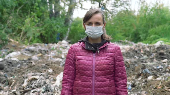 Woman in a Mask Standing Near the Garbage Pile alt