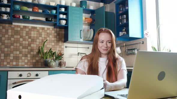 woman finishes work on laptop takes out pizza from box and eats with pleasure alt