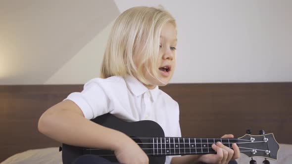 Distance Learning Online Education. A Cute Kid Boy Learning To Play the Ukulele and Singing on a