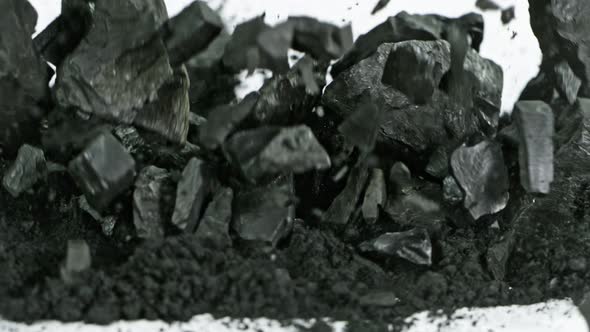Super Slow Motion Shot of Coal Falling Into Black Powder on White Background at 1000 Fps alt