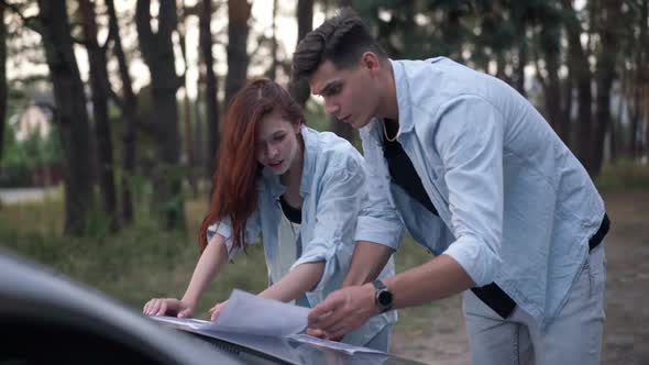 Positive Couple Talking Gesturing Examining Paper Map on Car Hood in Forest alt