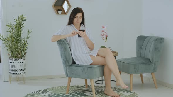 Beautiful  brunette  woman using smartphone leafing through social news relaxing on chair alt