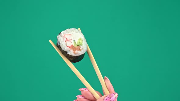Female Hands Hold Japanese Chopsticks with Sushi Rolls on Green Background alt