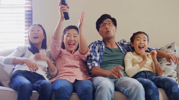 Excited family watching television together in living room 4k alt