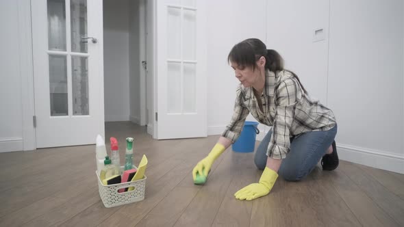 a housewife in yellow gloves is trying to clean the parquet with a brush and detergent.