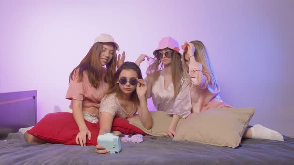 Four Happy Pretty Young Women in Pajamas Sits on Bed and Takes a Silfie on Vintage Camera in