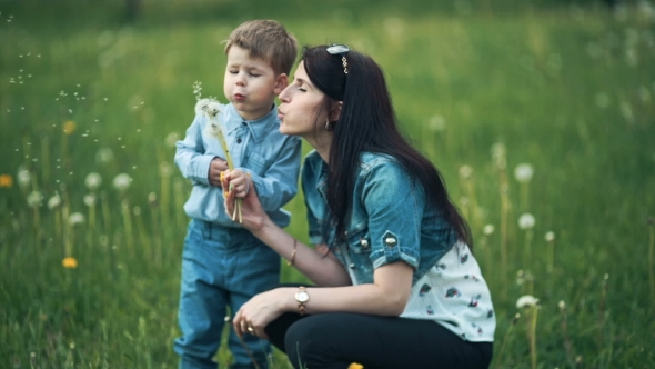 Mother And Child Blowing On a Dandelion In a Field