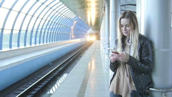Young Girl With Gadget Long Blonde Hair In Leather Jacket With Straightens Hair Standing In Metro alt
