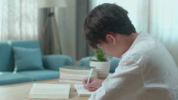 Asian Man Student Writing In Notebook On The Table While Studying At Home alt