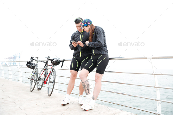 Couple with bikes using mobile phone on pier together - Stock Photo - Images