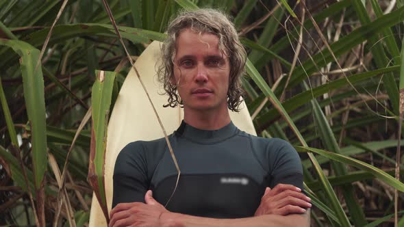 Surfer Stands Under Palm Tree with Arms Crossed on Chest