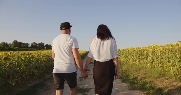 A Man And A Woman Walk Through A Sunflower Field Holding Hands