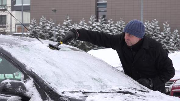 Man With Scraper Scraping Snow And Ice From Car Front Window In Winter. 