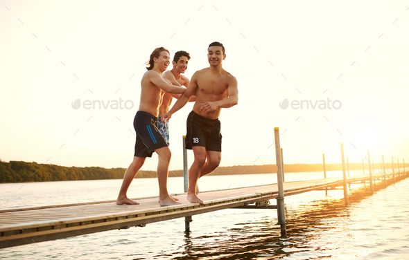 Two friends pushing a teenager into a lake - Stock Photo - Images