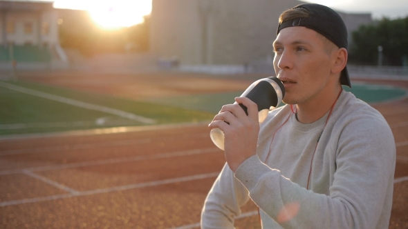 The Tired Athlete With Naseball Cap Drinks Water From The Bottle On Stadium Track