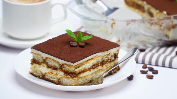 Traditional Italian Tiramisu dessert in glass baking dish, portion on plate and cup of coffee alt