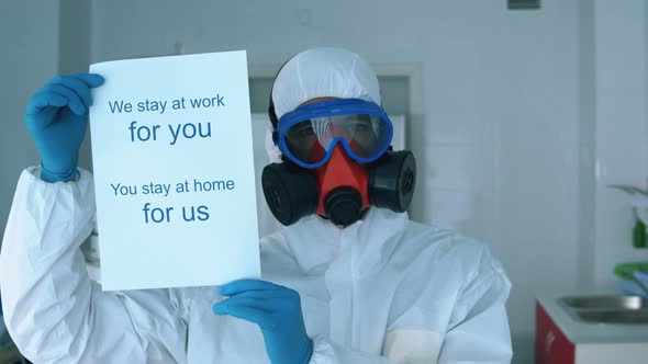 Specialist in a Protection Suit Is Asking To Stay at Home with a Poster alt
