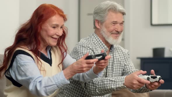 Cheerful Senior Couple 5060 Years Old Playing Football Using Video Game at Home Sitting on the Couch alt