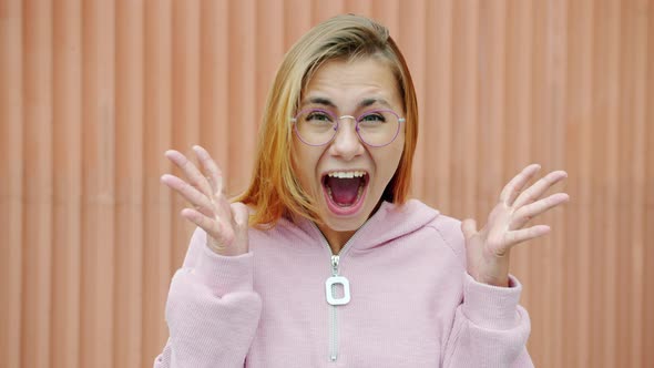 Slow Motion Portrait of Crazy Girl with Blond Hair Screaming and Raising Fists Looking at Camera alt