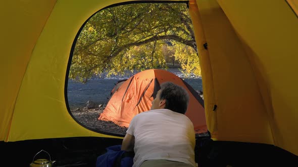 Back View of Adult Traveler in White T-shirt Looks from Open Tent, Altai