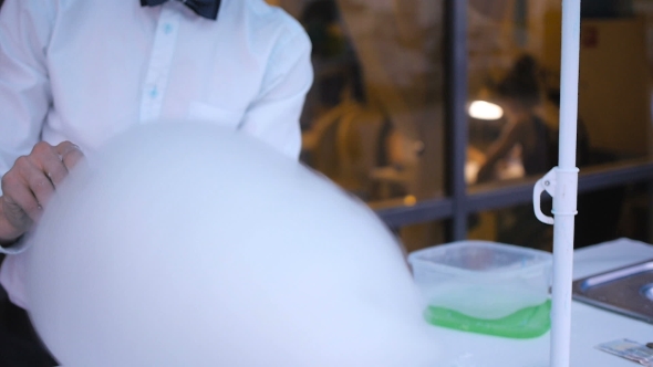 Young Guy Making Cotton Candy On a Special Machine, It Wears Bow Tie, Behind Him Balloons