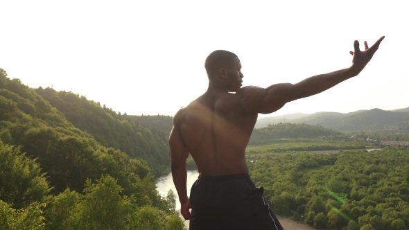 Back View. Muscular African American Athletic Man With Naked Torso Posing On The Rock