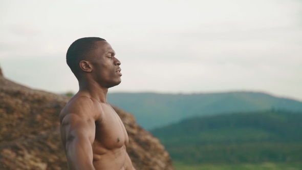 Side View Of Strong African American Bodybuilder Stretching Outdoor. Mountain Landscape Background