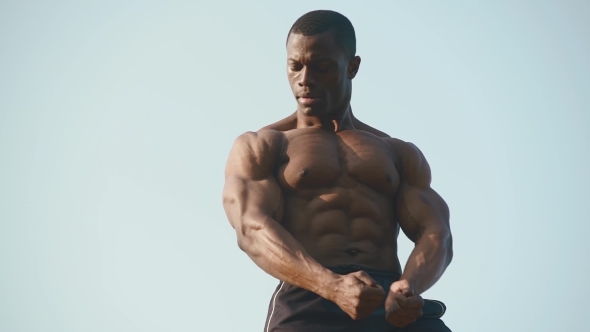 Strong Handsome African American Bodybuilder Showing His Perfect Muscles On The Clear Blue Sky