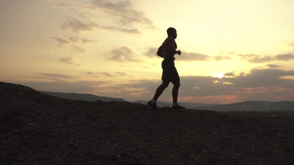 Silhouette Of African American Athlete Jogging On Sunset On The Mountain Peak