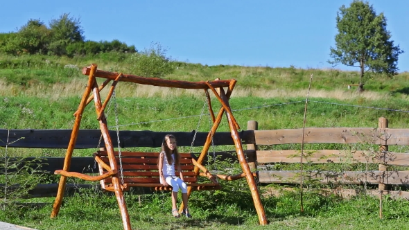 Little Girl Swaying On Wooden Chain Swing In Rural Playground