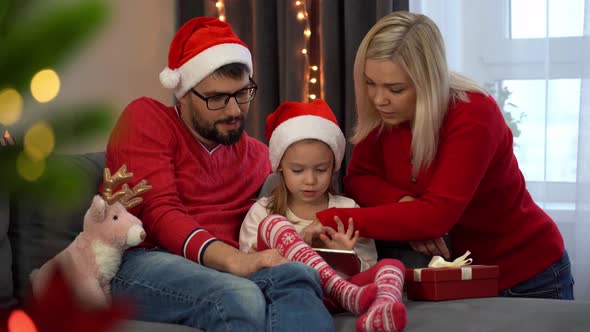 Family Choose Christmas Gifts in Online Store By Tablet Next to Christmas Tree