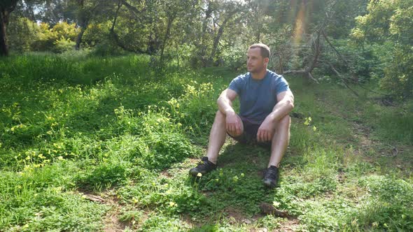 A handsome man sitting into a meditation pose in a green grassy forest meadow in nature on a bright alt