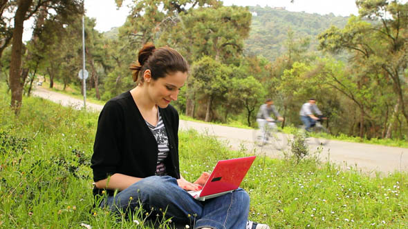 Beautiful Girl Using Computer in Countryside, Bicycles Passing Behind