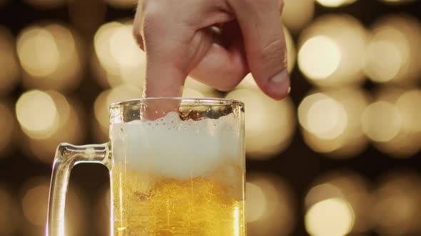Caucasian man stirs foam with a finger in a beer mug bokeh background close-up.